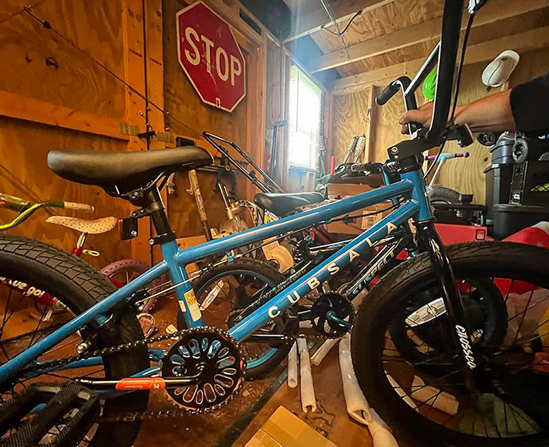 Blue kids' BMX bike with black tires parked in a wooden garage next to a vintage stop sign