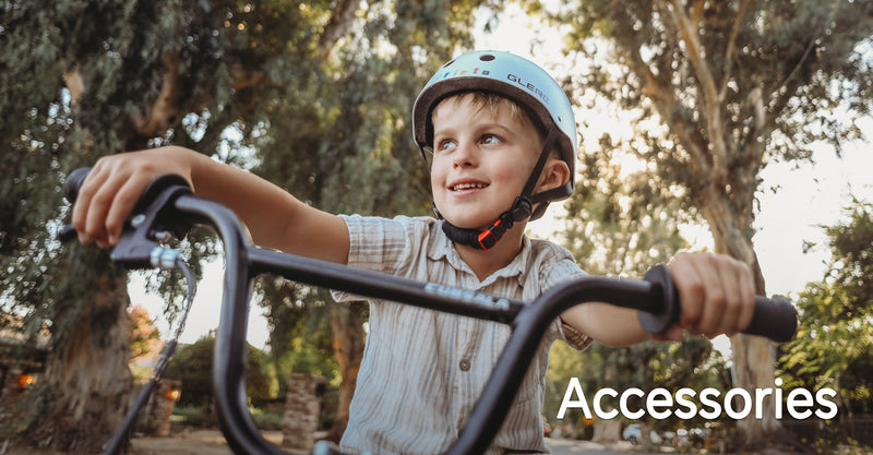Smiling boy in a blue safety helmet gripping bike handlebars outdoors among trees