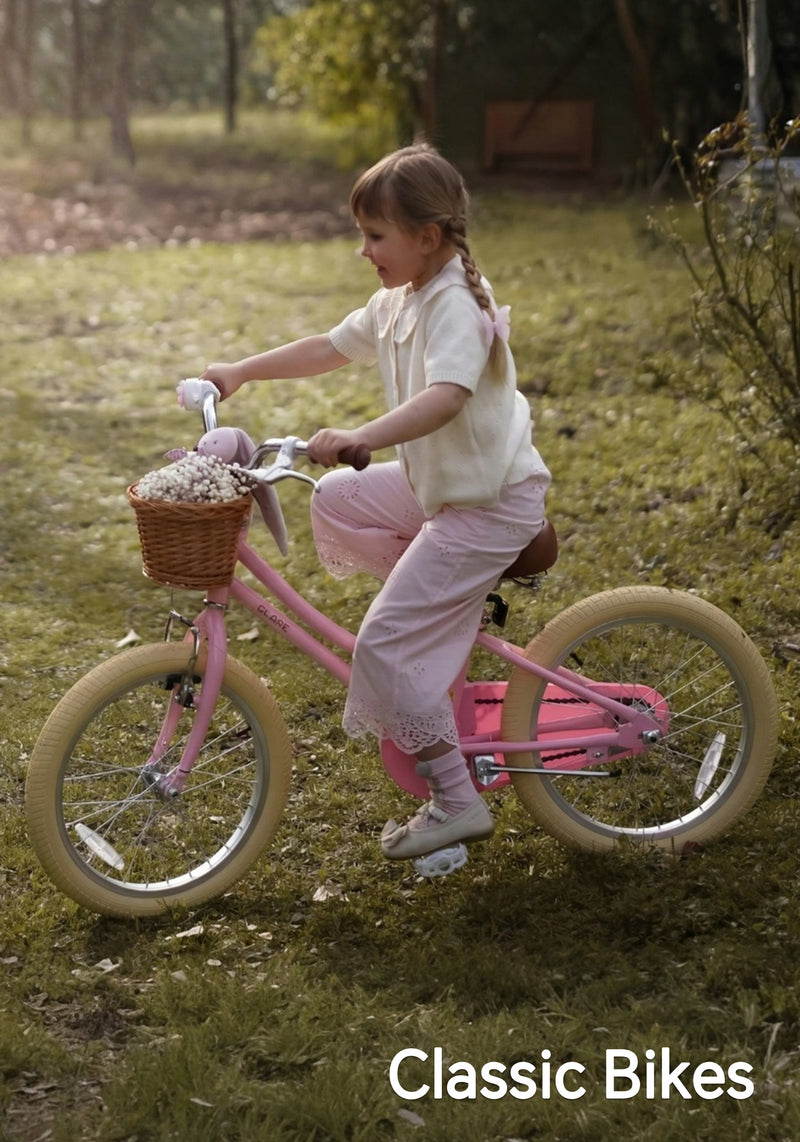 Young girl riding a pink classic bike with a wicker basket along a grassy park path